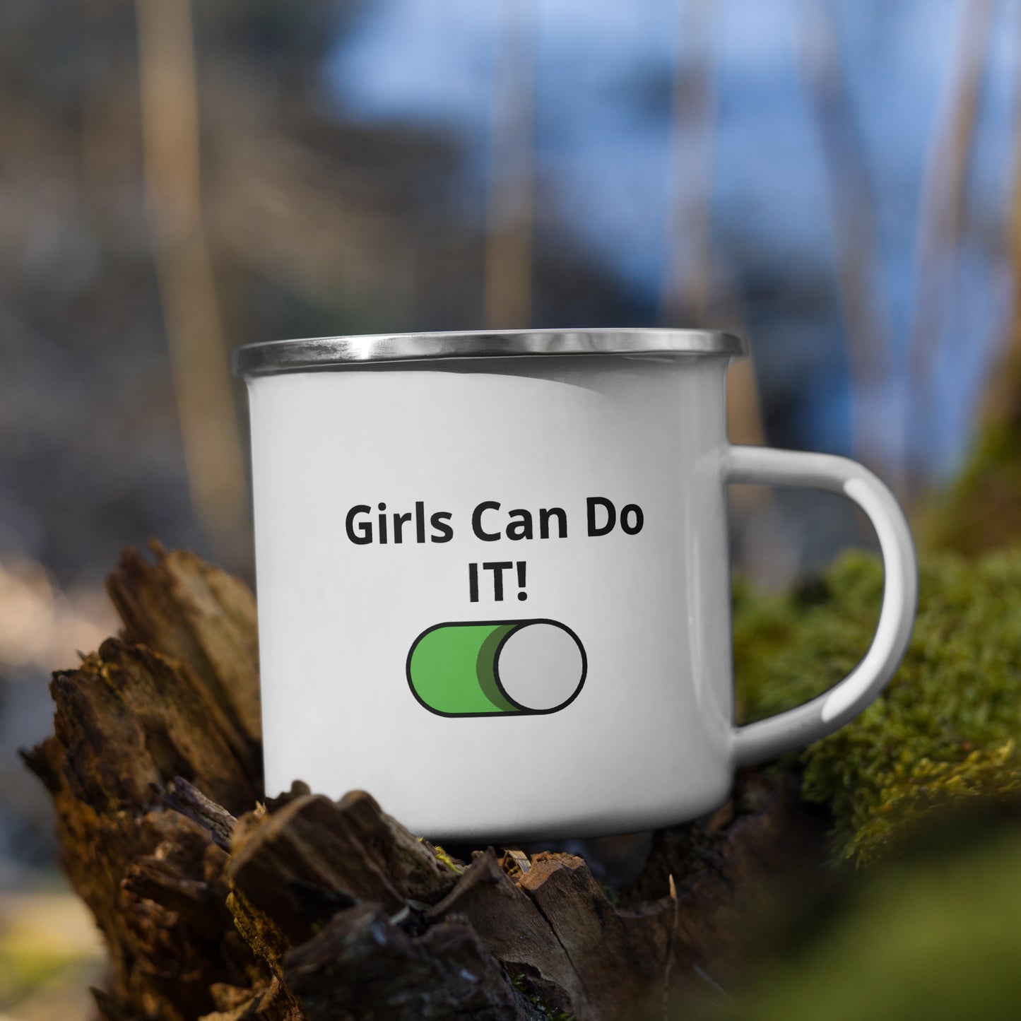 A white enamel mug with silver rim on a wooden surface, with 'Girls Can Do IT!' text and a green switch graphic printed on it.