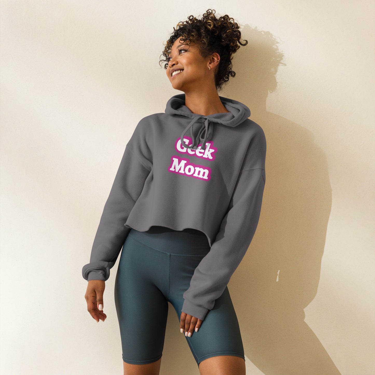 A woman wearing a gray crop top hoodie that says Geek Mom in a pink Barbiecore font.