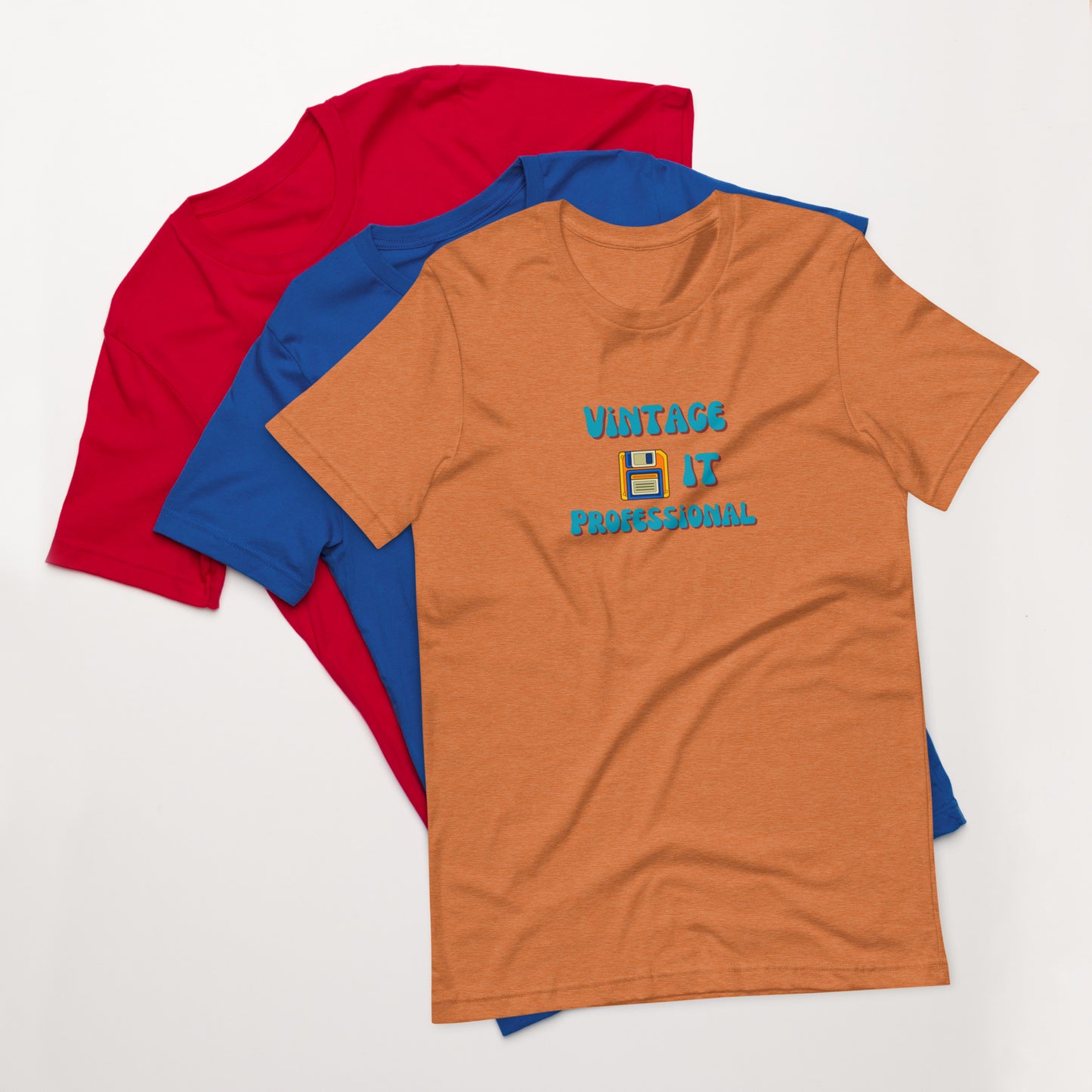 A stack of t-shirts with an orange one on top that says Vintage IT Professional and has a picture of a diskette on it.