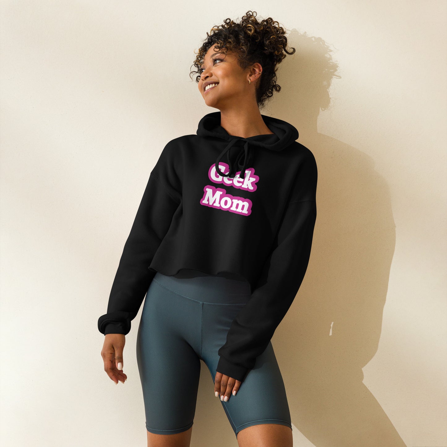 A woman wearing a black crop top hoodie that says Geek Mom in a pink Barbiecore font.